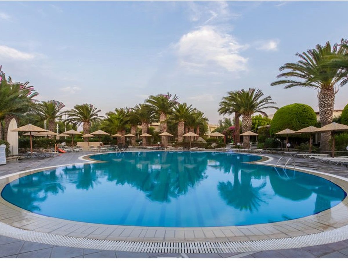 A large circular freshwater pool with a paved surround, thatched parasols and tall palms under a bright sky.