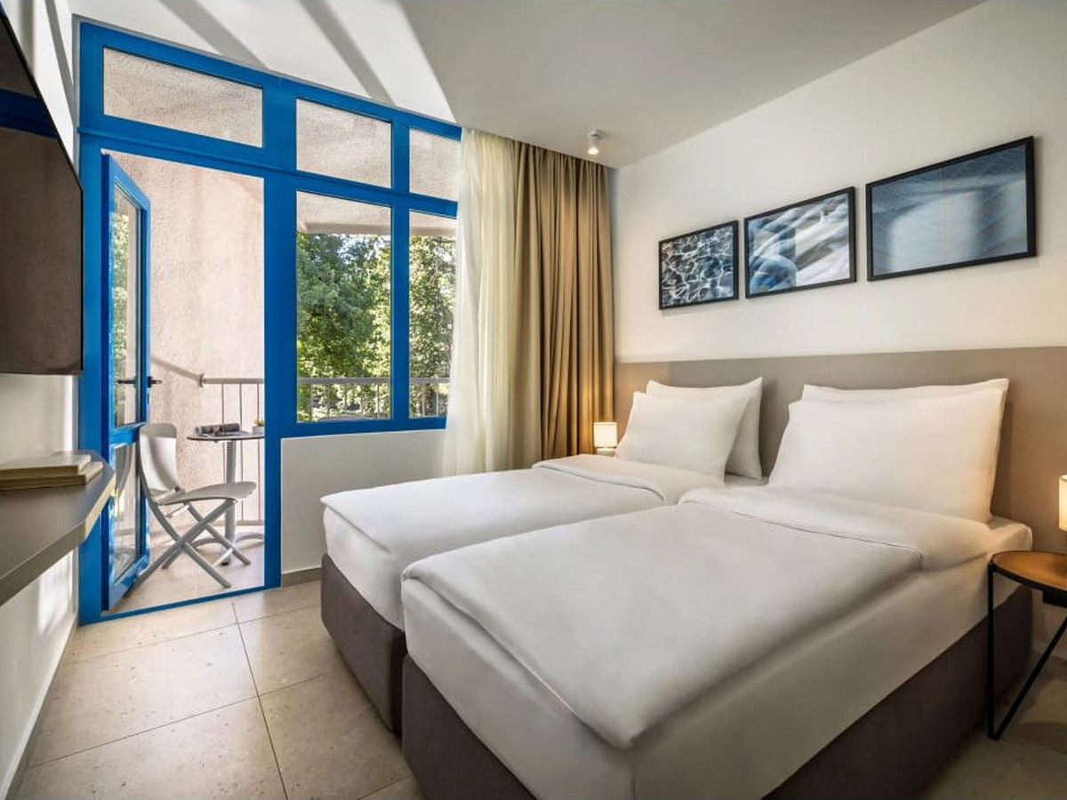 A double room with two single beds pushed together, framed prints and blue-framed balcony doors onto greenery.