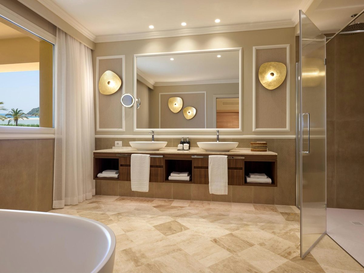 A spacious bathroom with twin basins on a double vanity, a freestanding bathtub by a window and a glass walk-in shower.