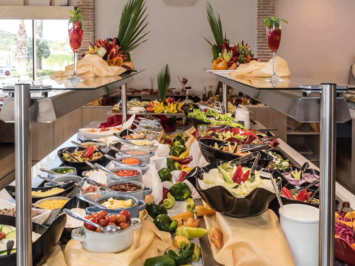 Buffet counter laid with salads, vegetables, dips and fruit under tall decorative fruit displays.