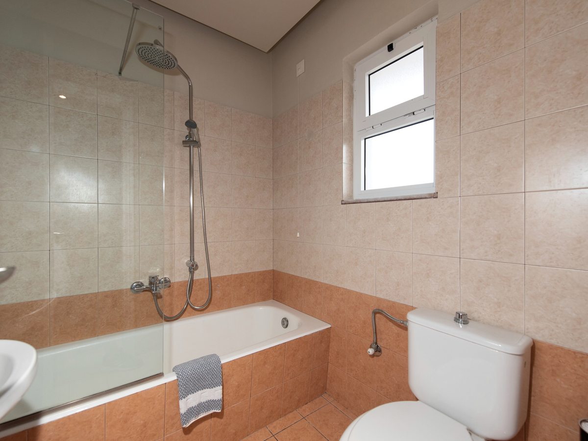 Bathroom with a bath and shower, a glass screen, a toilet and a basin, in beige and terracotta tiles.