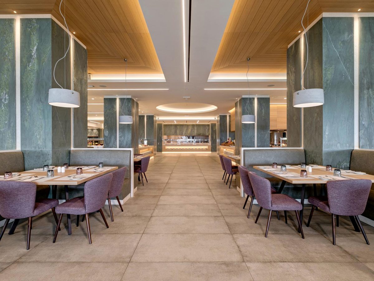 A large buffet restaurant with green marble columns, purple upholstered chairs and booth seating, a timber-panelled ceiling and a buffet counter at the far end.
