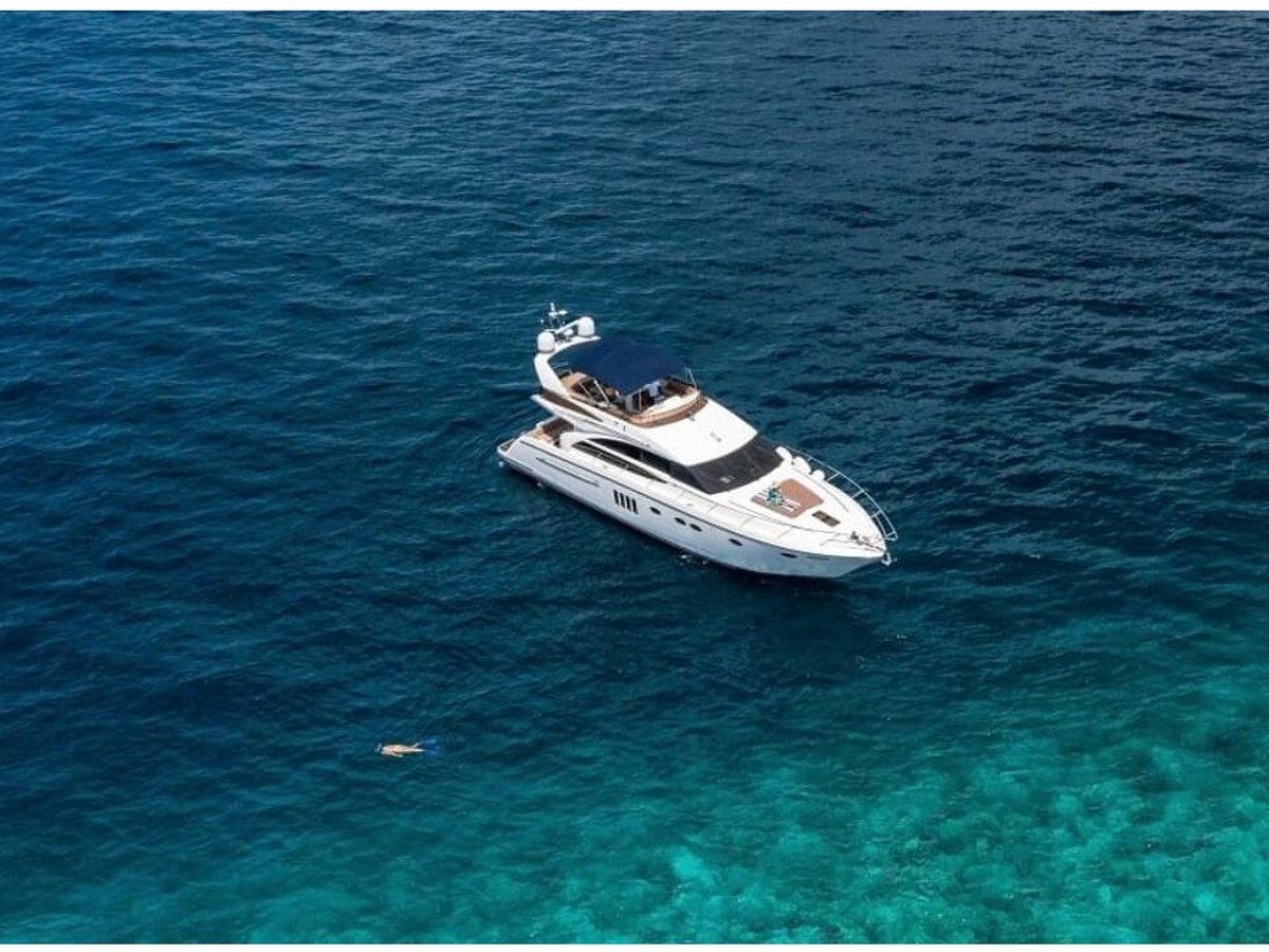 A white motor yacht anchored in clear turquoise water over a pale sand seabed.