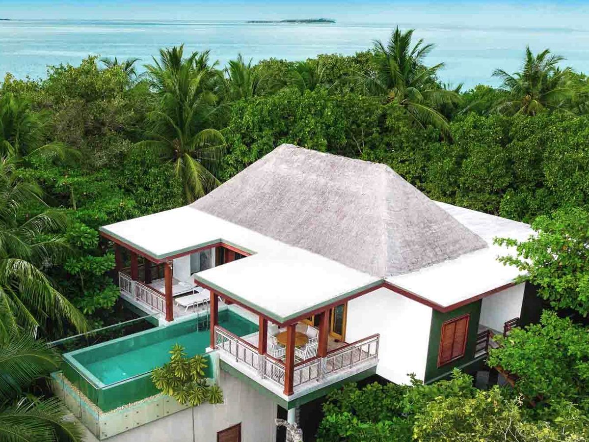 A two-storey villa with a thatched roof and wraparound balconies, raised among palms and dense greenery, with a plunge pool alongside.