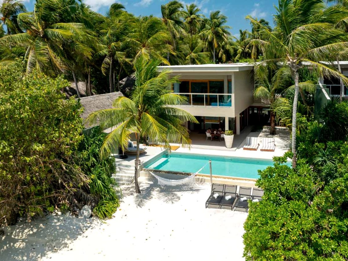 A large two-storey beachfront residence among palms with a private pool on its sandy terrace beside the lagoon.