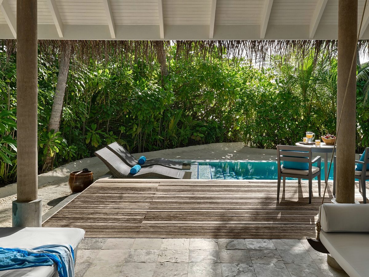 A private plunge pool on a covered villa terrace with two sun loungers, an outdoor dining table and dense garden planting around the deck.