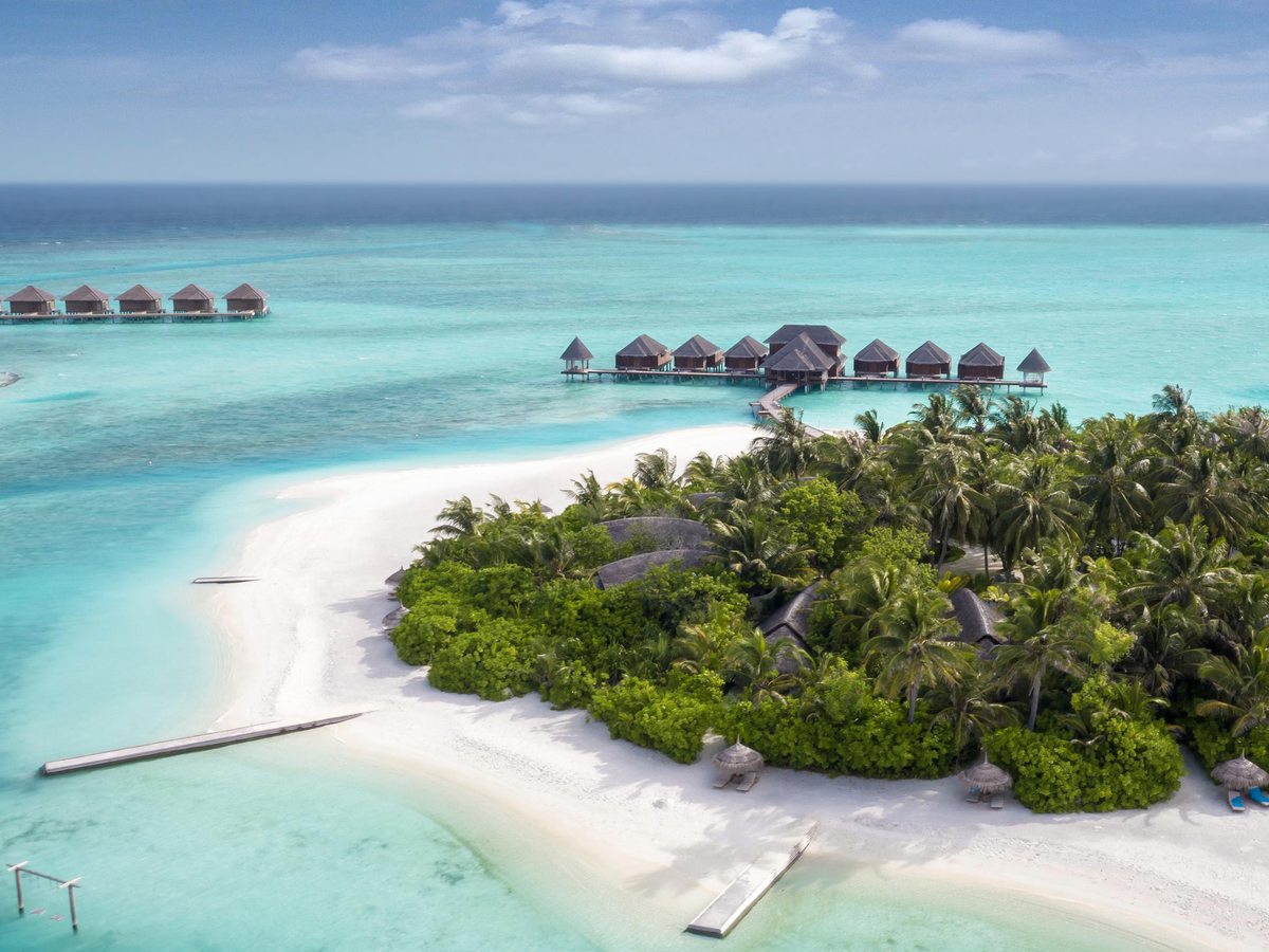 Aerial view of the island's white-sand beaches and a sandbar curving into a shallow turquoise lagoon dotted with overwater villas.