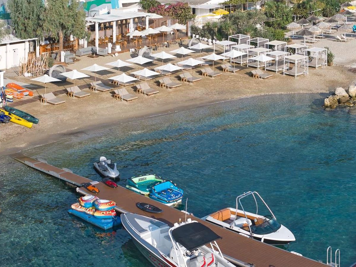 An aerial view of a timber jetty off the beach with kayaks, paddle craft and small motorboats moored in clear shallow water.