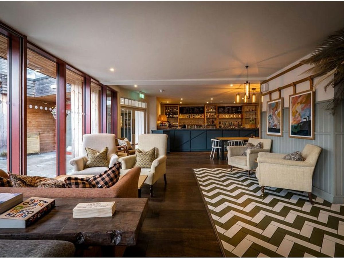 A lounge and bar with armchairs, a chevron rug, a herringbone floor, a blue bar counter at the back and glazed doors to a terrace.