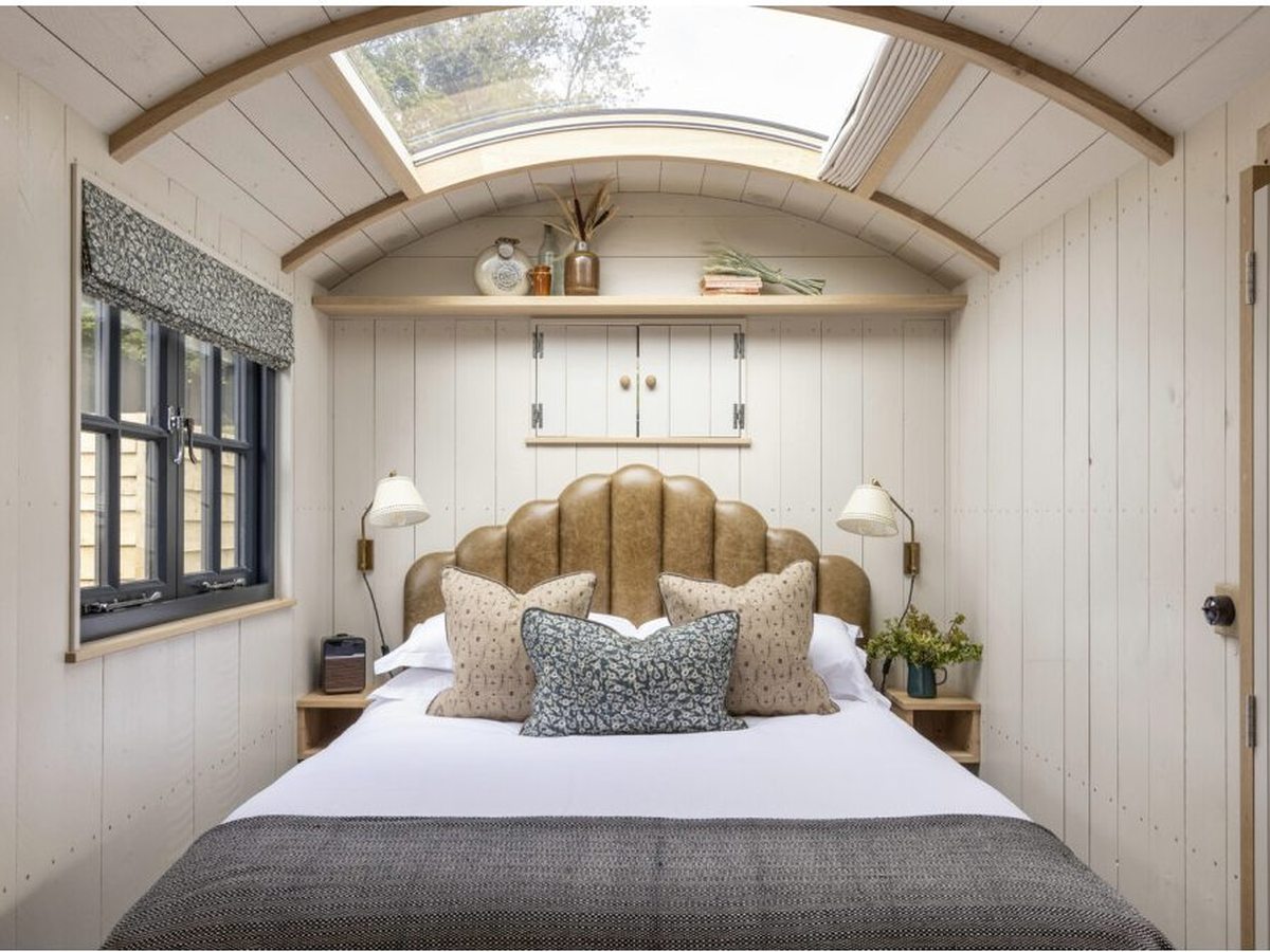 A compact wood-panelled hut interior with a curved ceiling, a skylight over the bed and a small shuttered window.