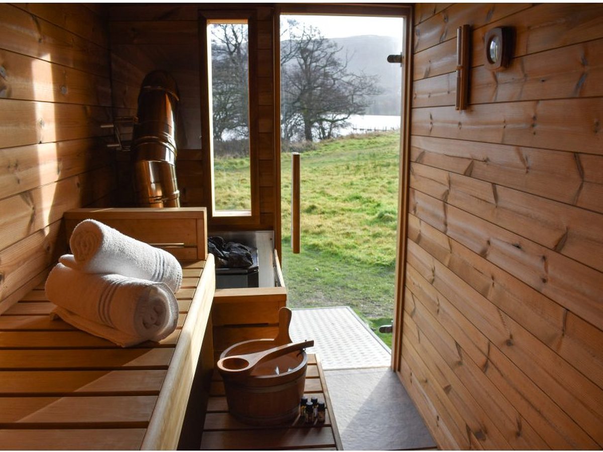 A timber-lined sauna with a folded towel on the bench and glazed doors open to grass and the lake.