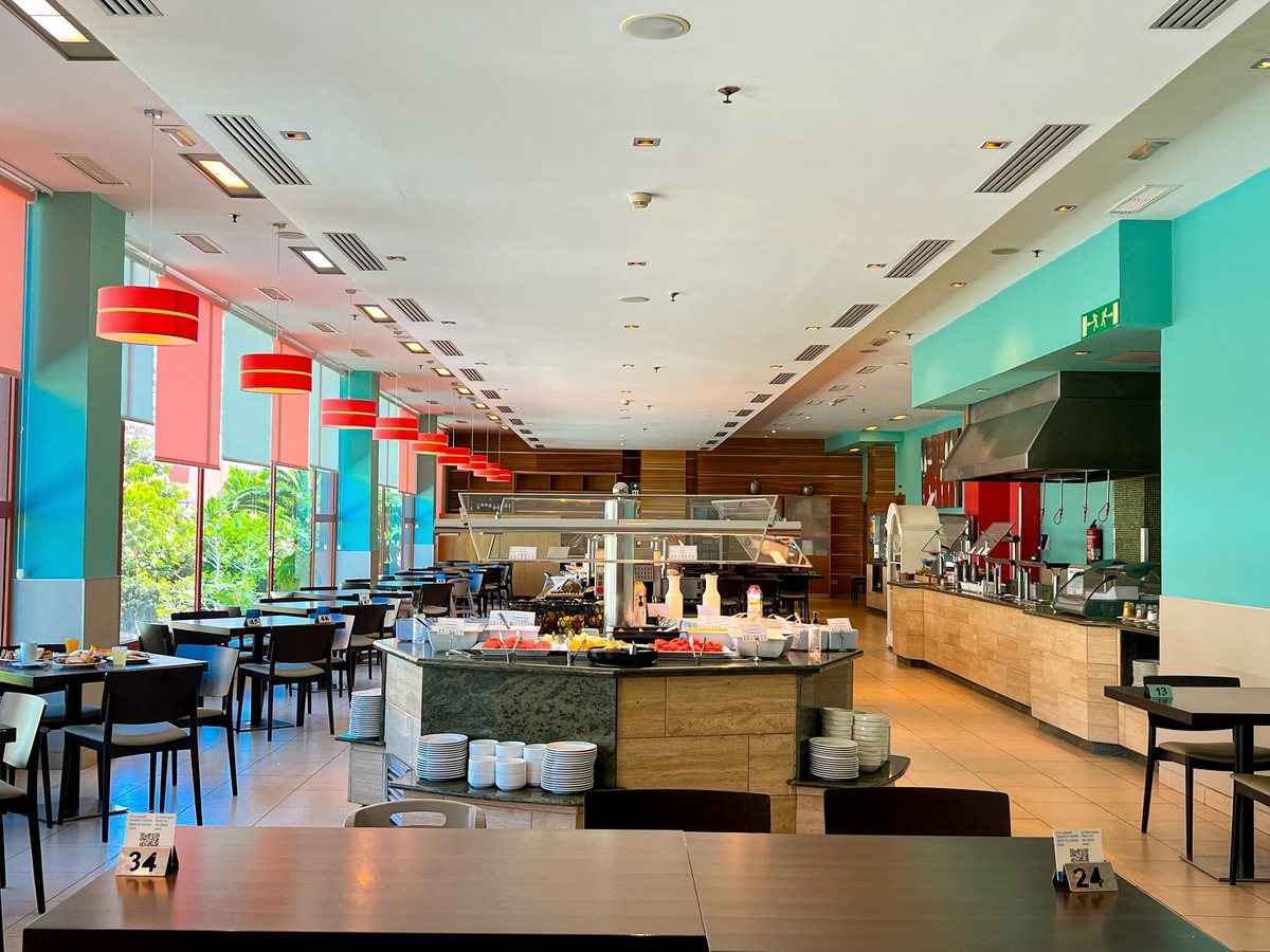 A self-service buffet island with hot counters and staff, in a bright dining room with tall windows onto the pool.