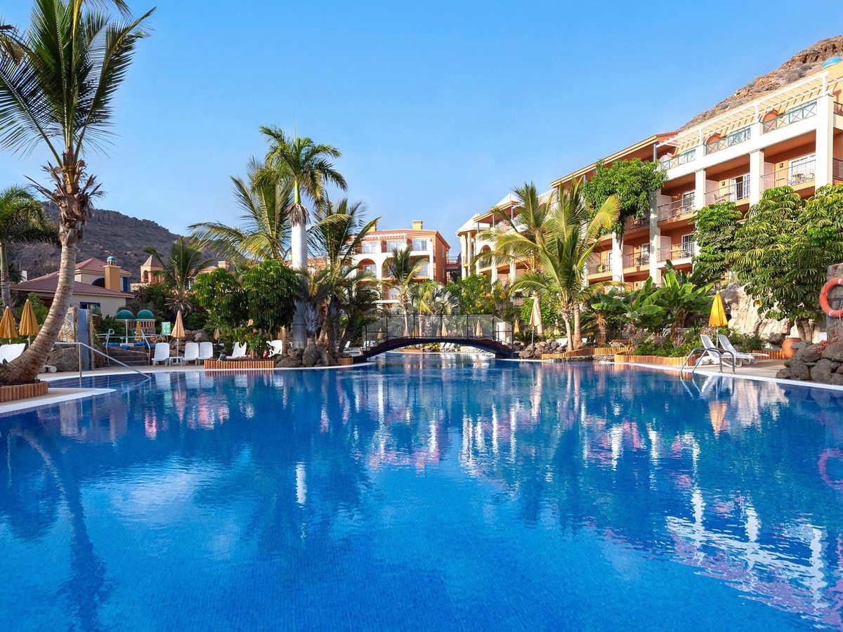A large curving pool with an arched footbridge, palm trees and the salmon apartment blocks behind.