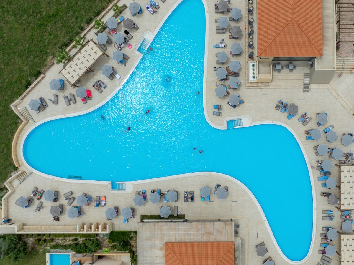 An aerial view of a large freeform lagoon-shaped pool with sun loungers, parasols and pavilions around its curved edges.
