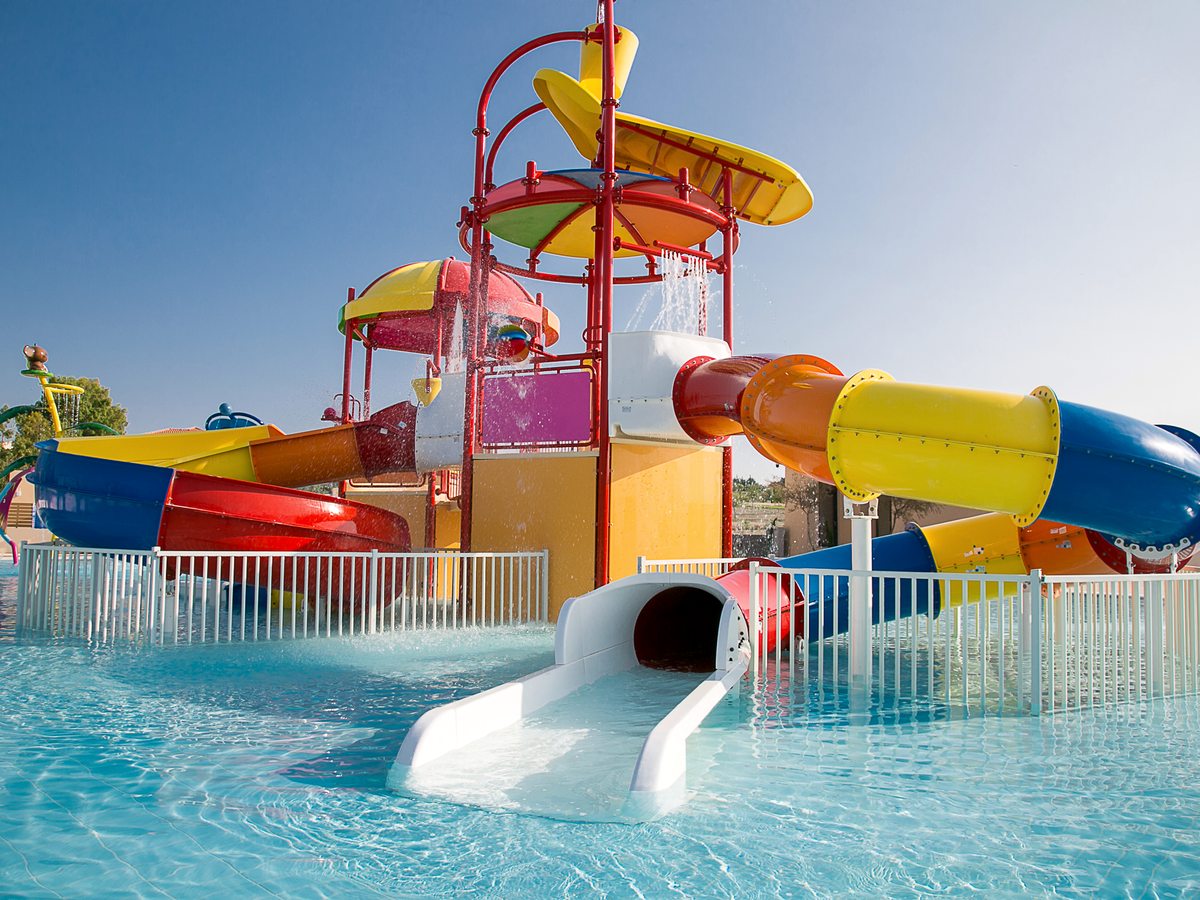 A tall multi-coloured water-slide tower with looping tube slides ending in a shallow splash pool.