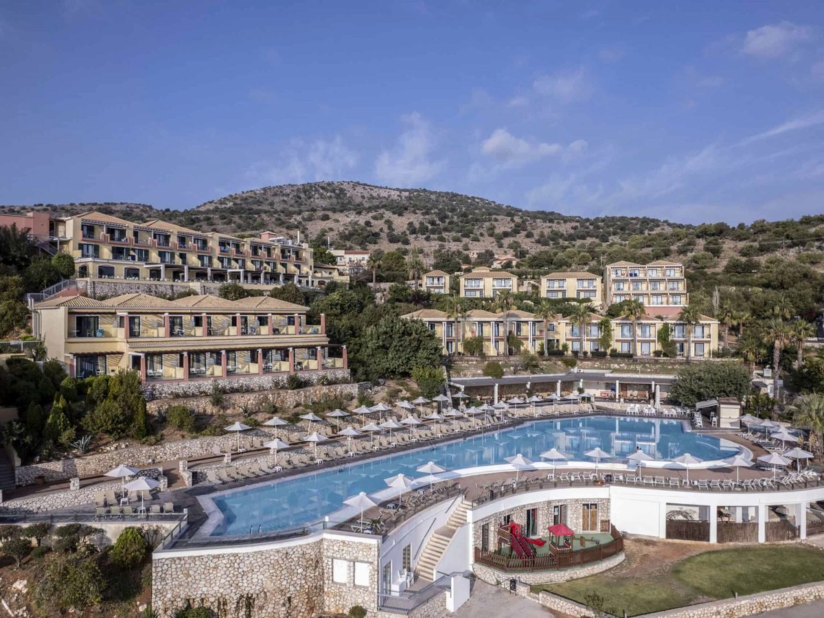 The main pool ringed with white parasols, with the resort's rooms rising up the hillside behind.