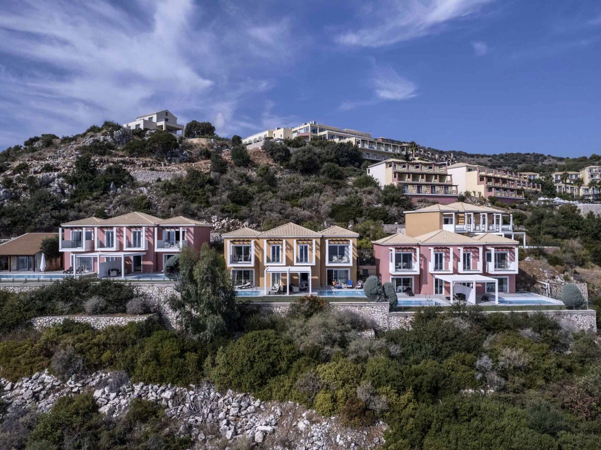 Rows of peach and cream buildings with balconies set into a rocky, planted hillside.