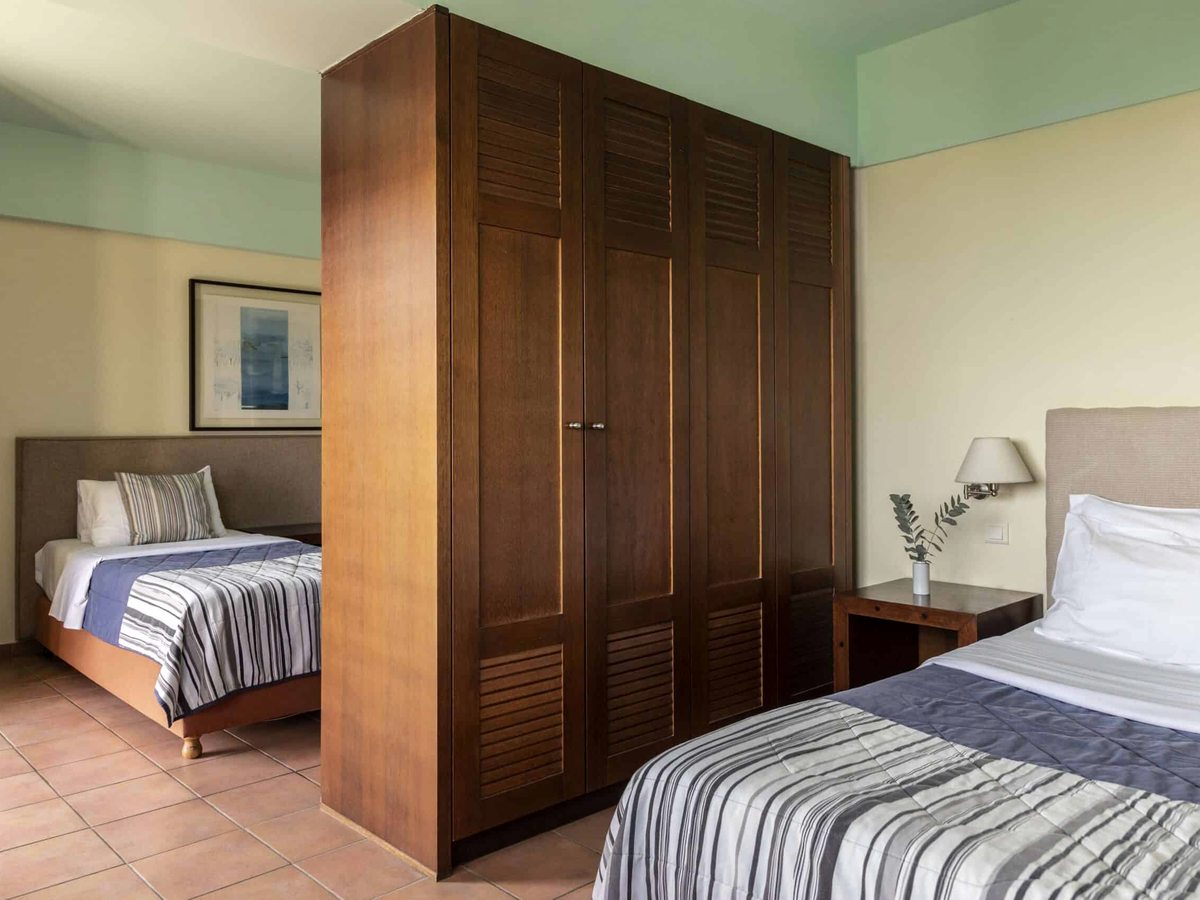 A single bed beside tall wooden wardrobes that partition off a separate sleeping area, with striped covers.