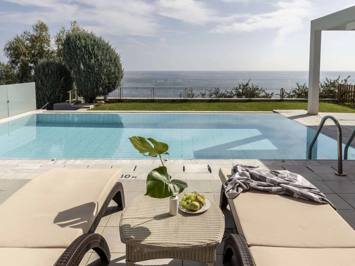 A private rectangular pool on a paved terrace with two sunloungers and a low table, a grass strip and the sea beyond.