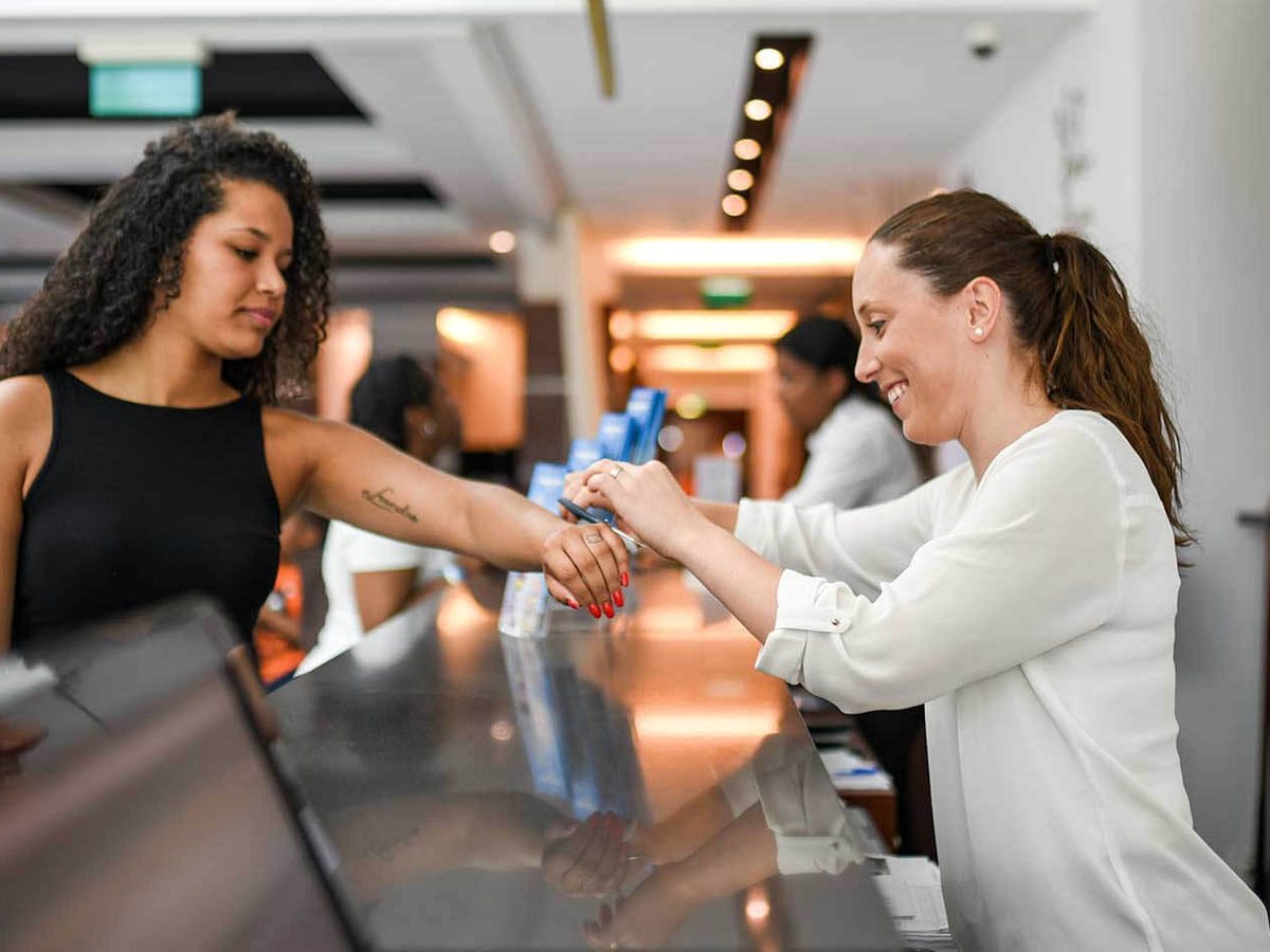 Two staff at the hotel reception desk fitting a wristband to a guest at the check-in counter.