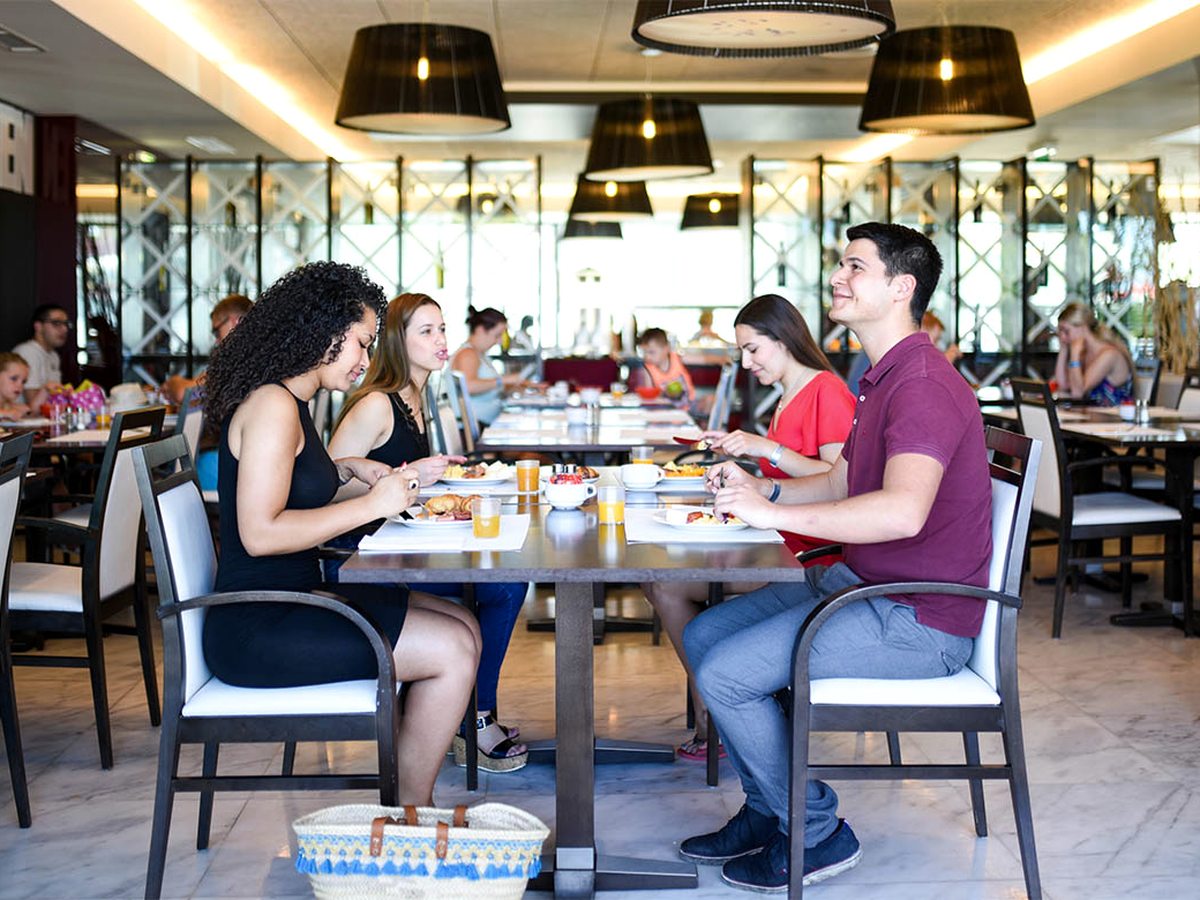 Diners at tables in the Charme Restaurant under black pendant lamps, with mirrored panels and a tiled floor.