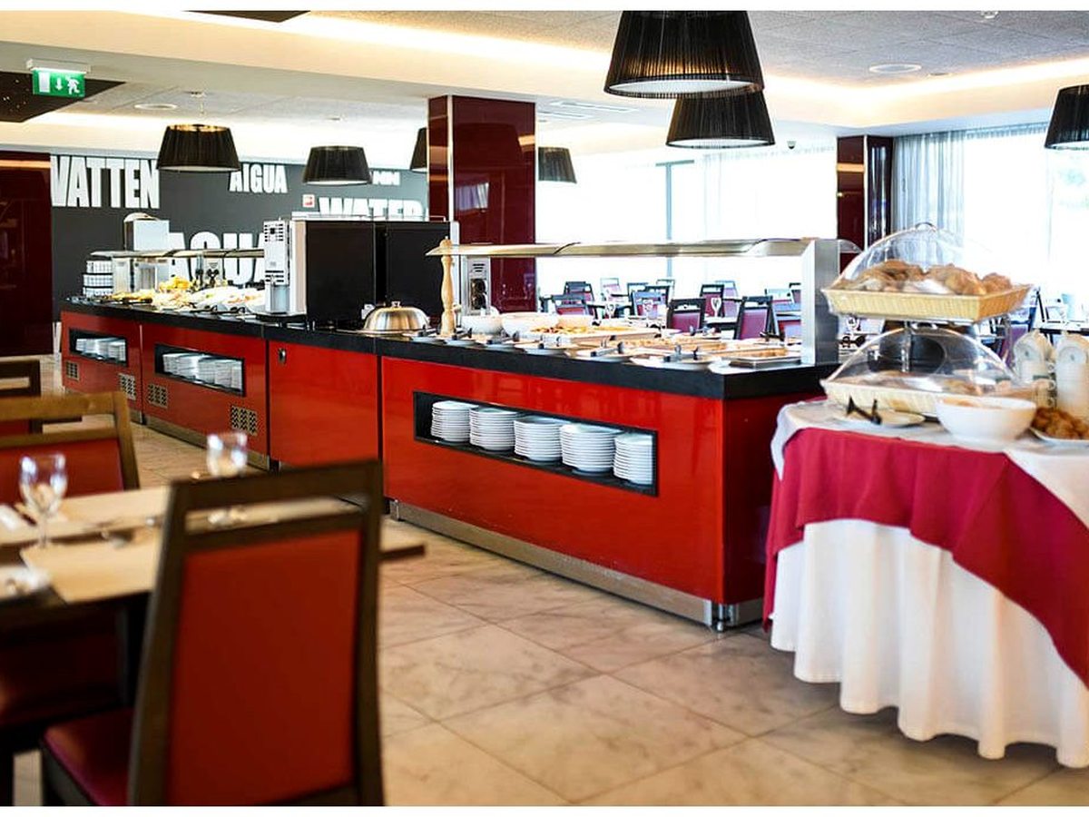 A breakfast buffet with red counters, bread and pastry displays and stacked plates.