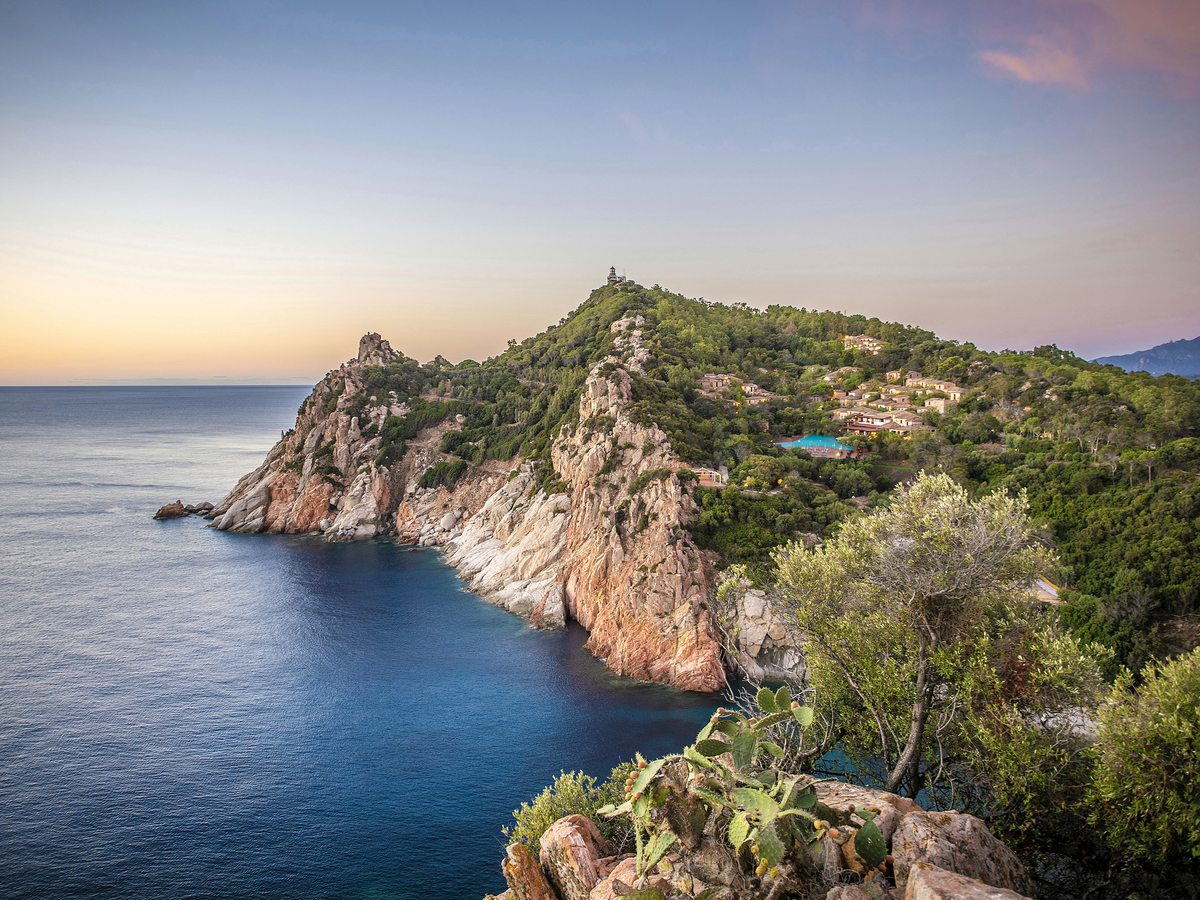 A tall red-rock cliff headland covered in green scrub dropping to deep blue sea.