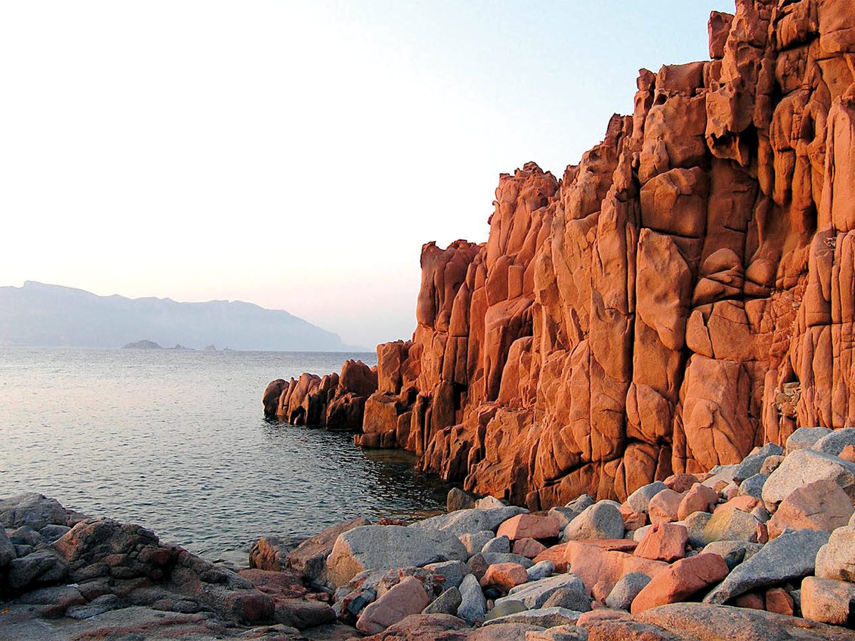 Jagged red porphyry rocks meeting clear blue sea on the coast at Arbatax.