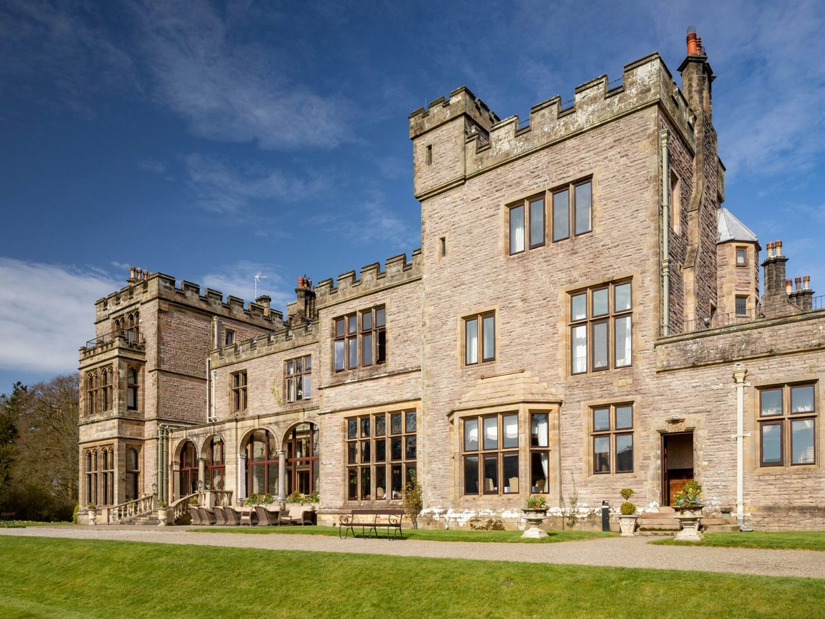 The castellated stone front of Armathwaite Hall against a blue sky, with a lawn in front.