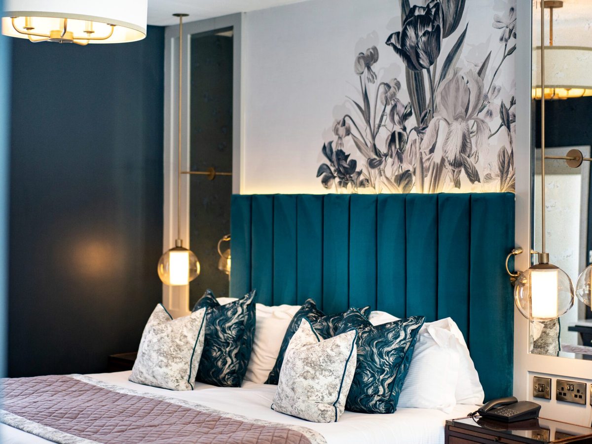 A double bedroom with an upholstered teal headboard and a floral wall behind the bed.