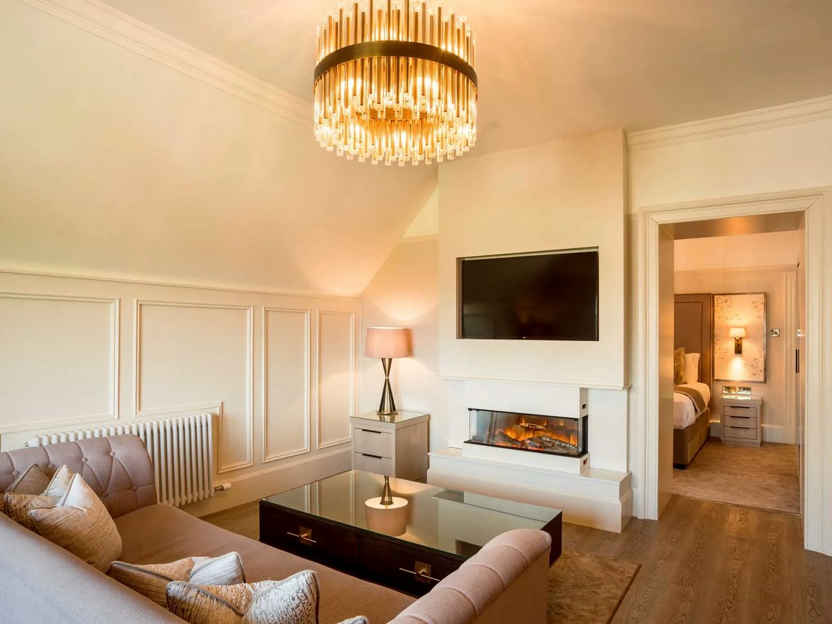 A suite lounge with a sofa, coffee table, wall-mounted television and a modern fireplace.