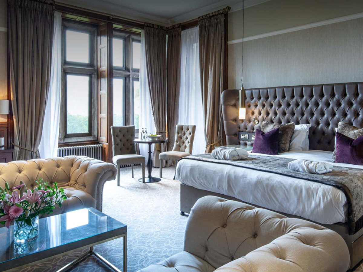 A spacious suite with a tufted-headboard bed, armchairs and a bay window looking onto the grounds.