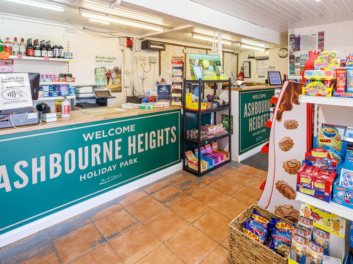 A reception and shop counter beneath a green Welcome to Ashbourne Heights sign, with sweets, snacks and a card payment terminal.