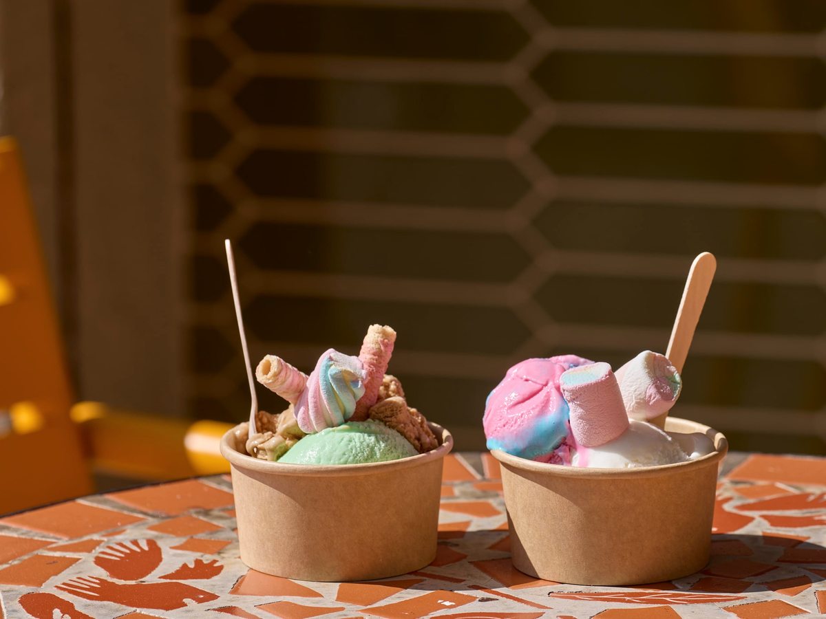 Two tubs of colourful gelato with wafer sticks on an orange patterned table.