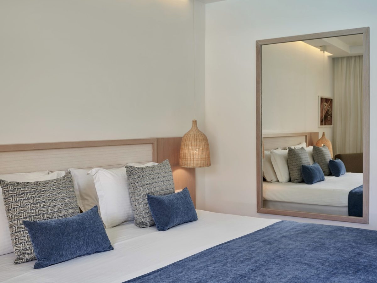 Double room with a timber headboard, white linen and a blue throw, a woven pendant light and a wall mirror.