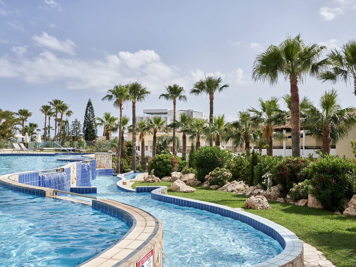 Ground-level view of the blue-tiled lagoon pool curving past tall palms, planted borders and low resort buildings.