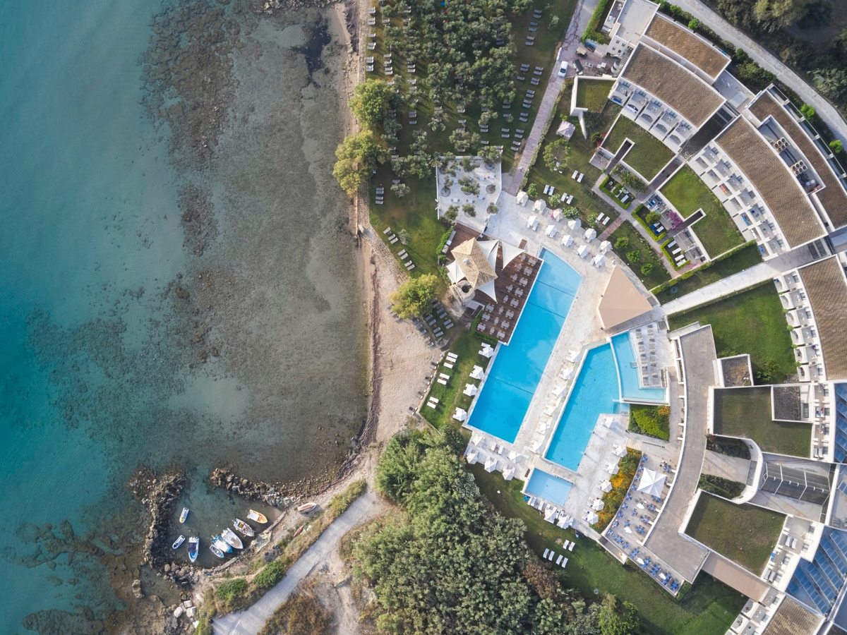 Overhead aerial of the resort's pools and buildings beside a sandy beach and clear turquoise shallows.