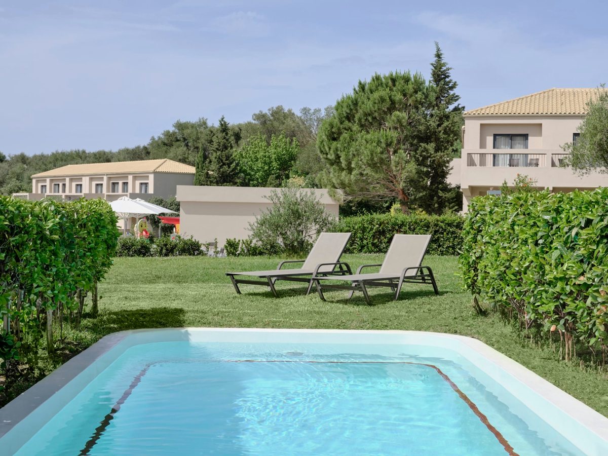 A rectangular turquoise pool set in lawns beside a low guest block, with a pair of loungers on the grass.
