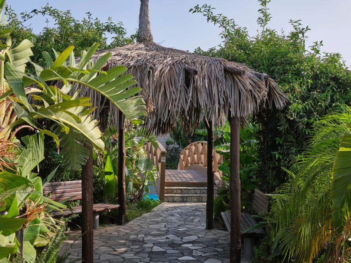 Stone walkway winding through lush tropical planting and palms to a thatched shelter in the resort grounds.