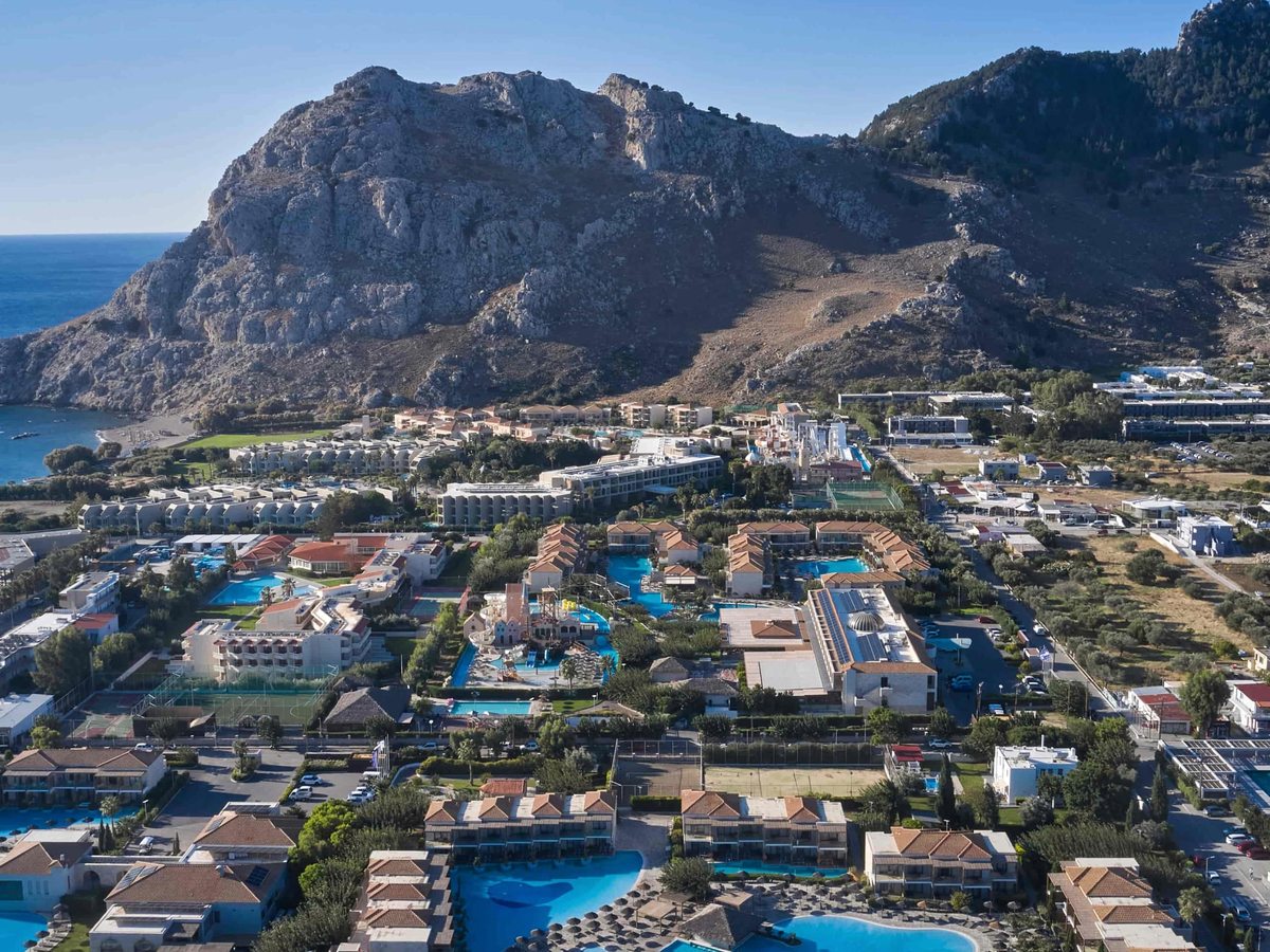 Aerial view of the resort's low-rise blocks with pitched roofs among landscaped grounds and pools, a football pitch and the sea in the distance.