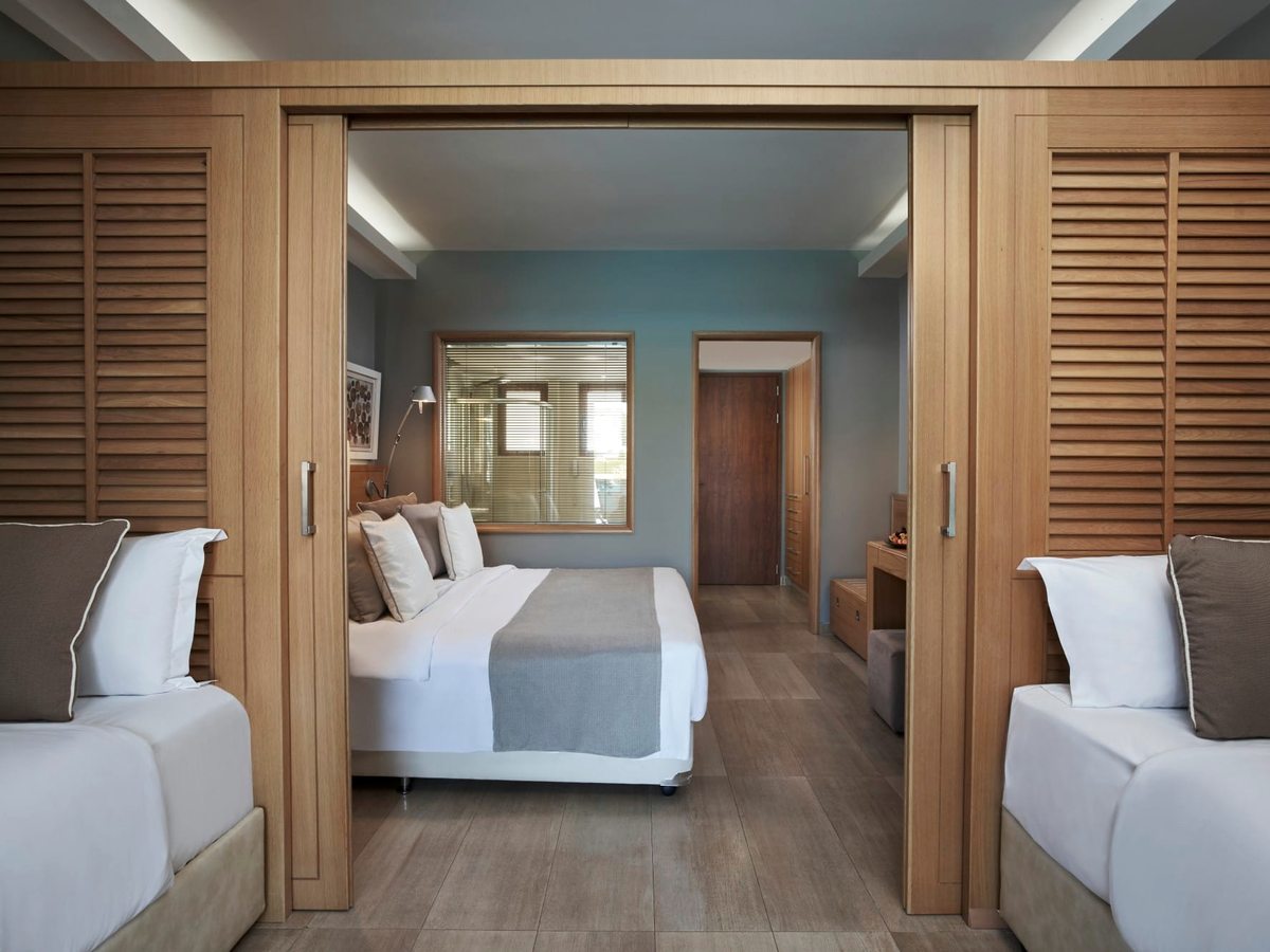 Suite bedroom with a double bed flanked by sliding louvred wooden partitions opening to single beds on either side.