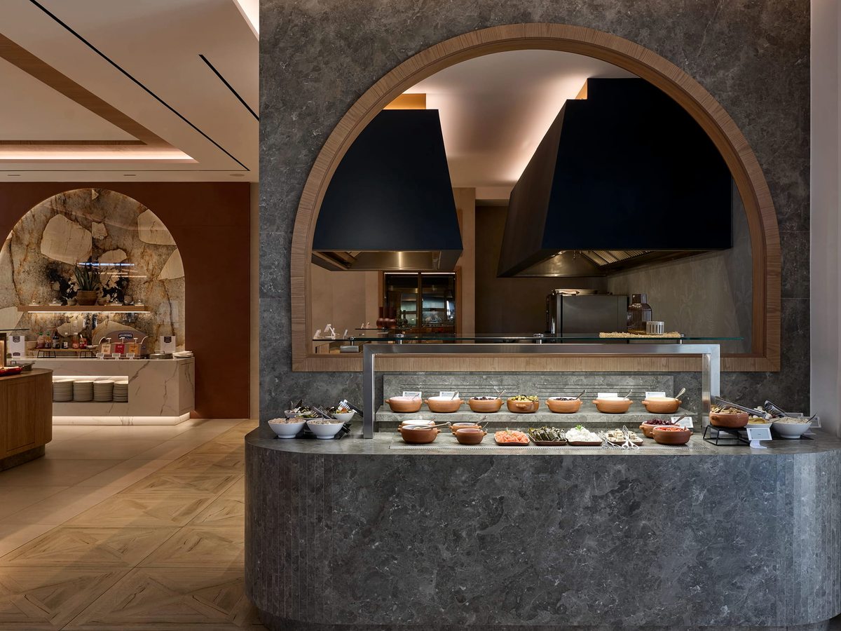 Indoor buffet with an arched stone show-cooking station and a curved counter of dishes and pastries under warm lighting.