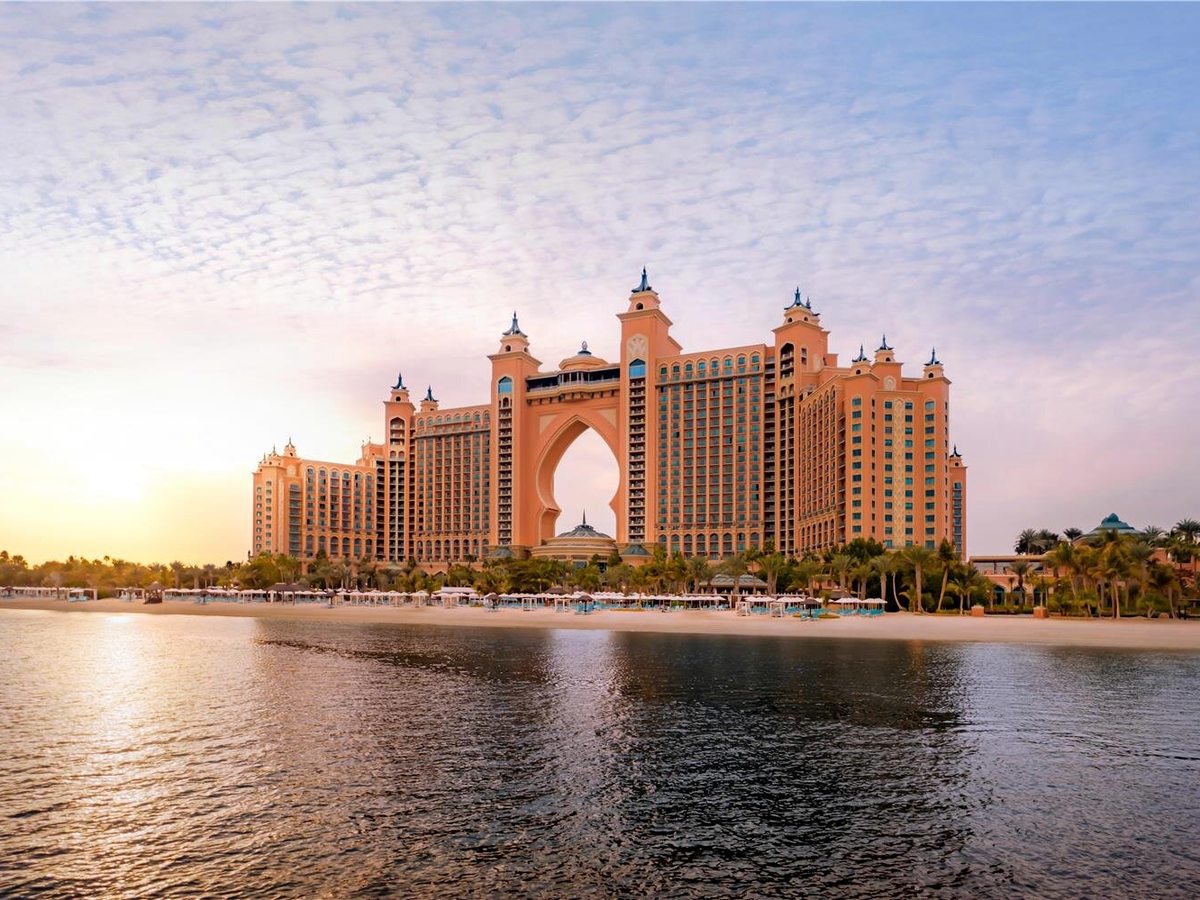The salmon-pink resort seen from the sea, its two towers linked by a tall central arch, with the shoreline in front.