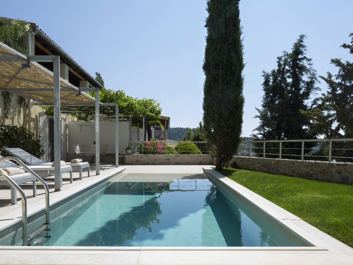 A rectangular garden pool with sun loungers under a pergola, a lawn and a cypress tree, in sea-facing grounds.