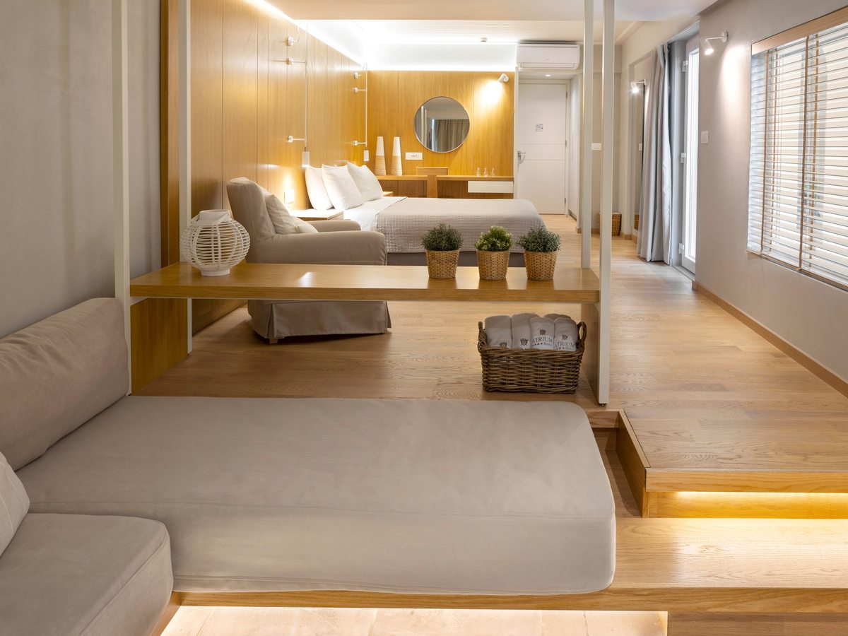 A suite with a lower cushioned daybed area and an LED-lit step up to a raised bedroom with a wood-panelled wall and a round mirror.