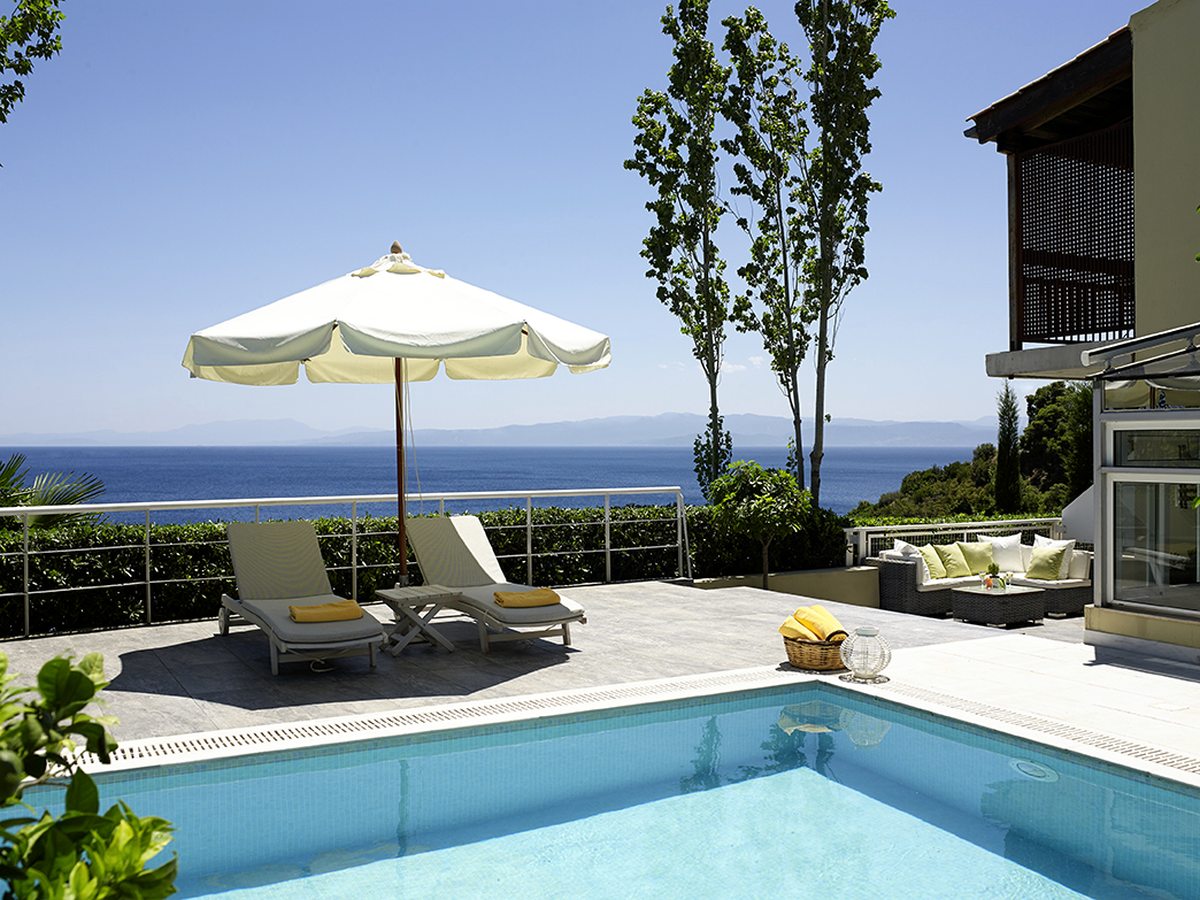 A private pool on a suite terrace with sun loungers, a parasol and an outdoor sofa behind a glass railing, with a sea view beyond.