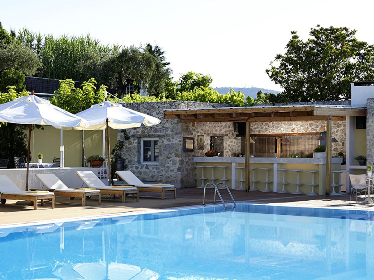 A stone-built poolside bar with a covered counter, sun loungers and white parasols along the pool deck with greenery behind.