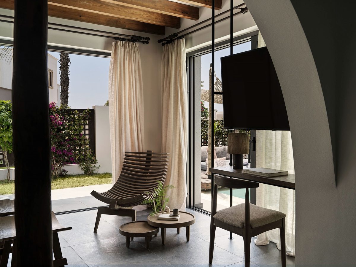 Room seating corner with cane chairs and a low table beside sliding doors, a private pool and garden outside and a wall-mounted TV opposite.