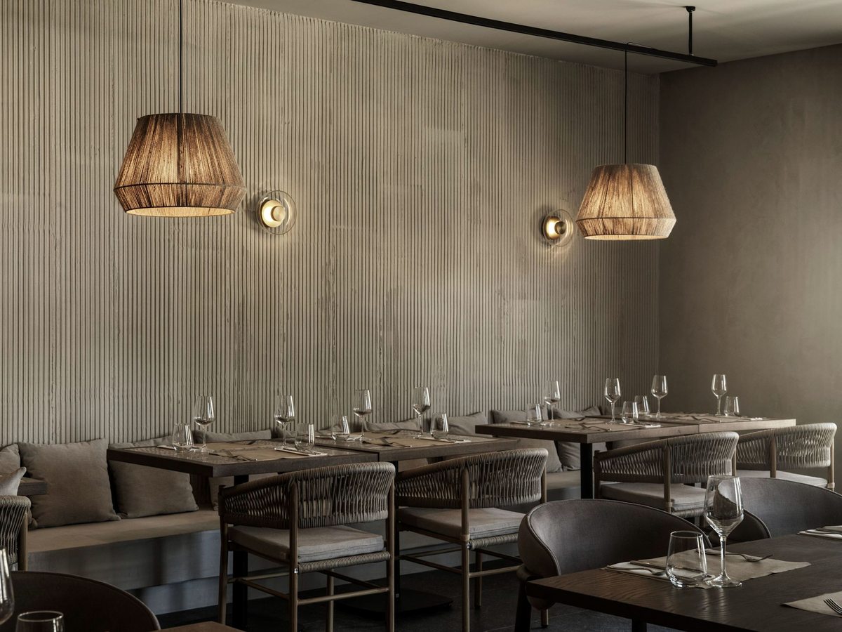 Indoor restaurant with set tables, banquette seating and woven pendant lights along a panelled wall.