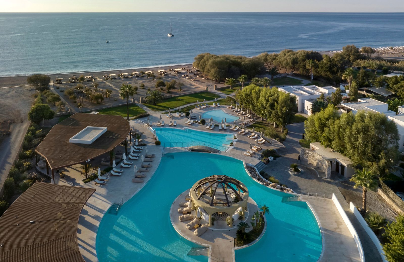 Aerial view of the resort's curved main pool and grounds above the beach and calm sea at Lardos, on the southeast coast of Rhodes.